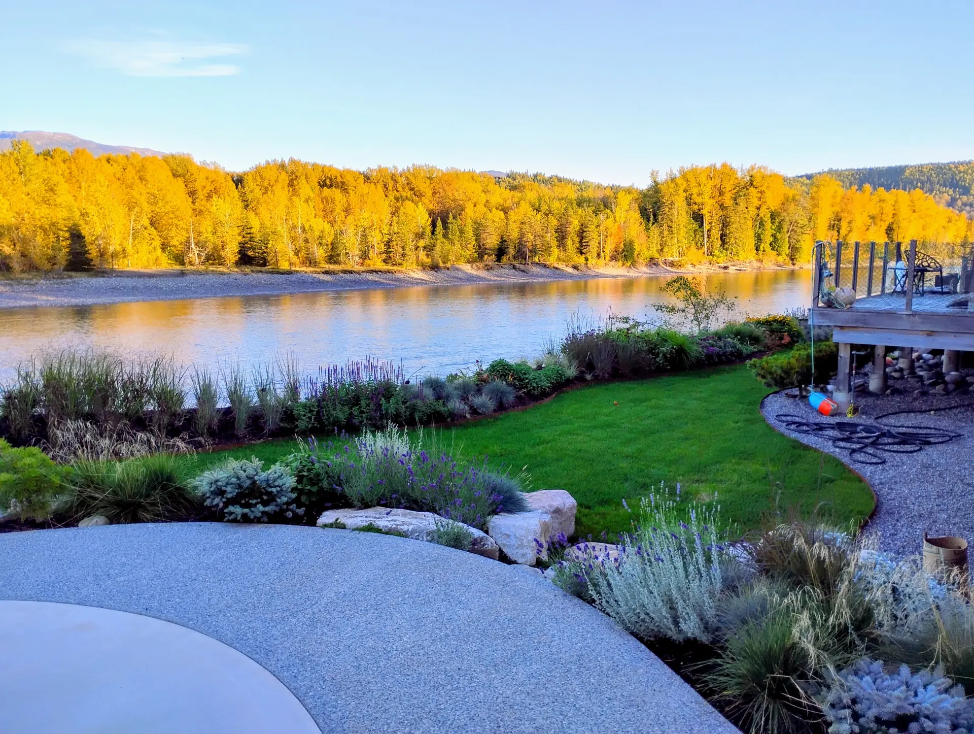 A green lawn and planted borders running down to the river, with yellow autumn trees on the far bank