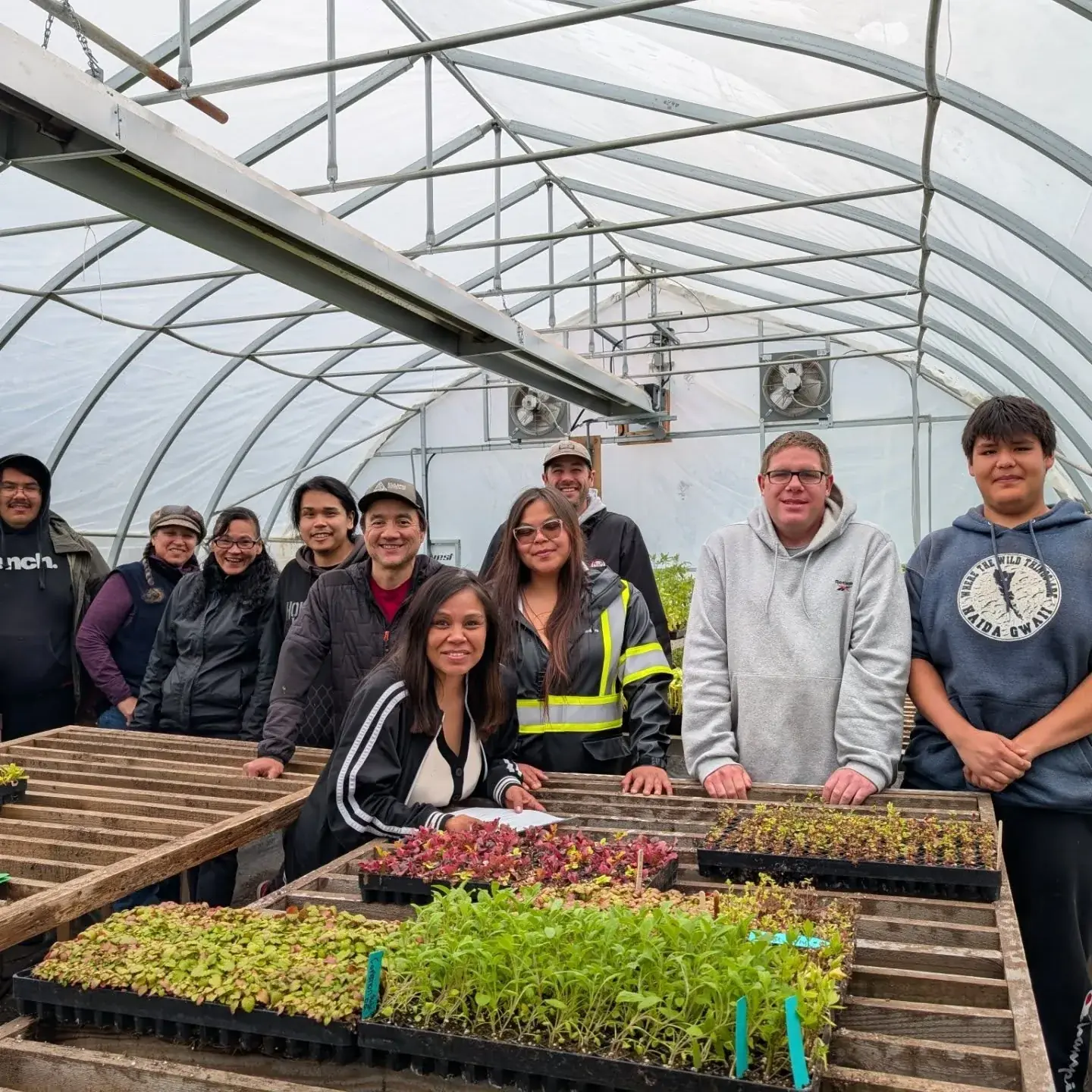 A graduating class gathered around benches of seedling trays inside the greenhouse