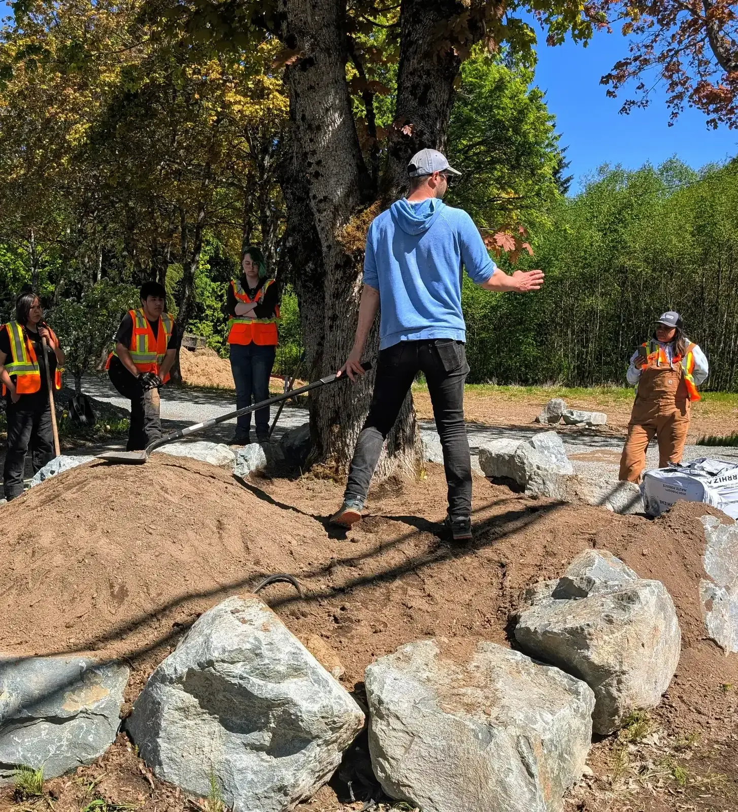Wesley talking a group of hi-vis students through the boulder beds under a large maple