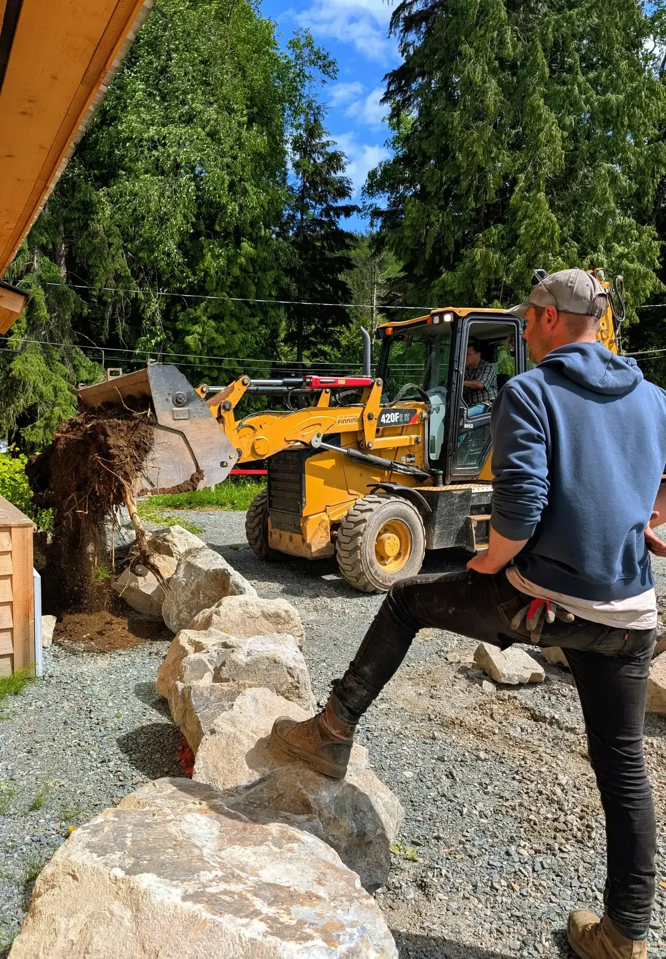 Two people discussing placement beside a loader carrying boulders