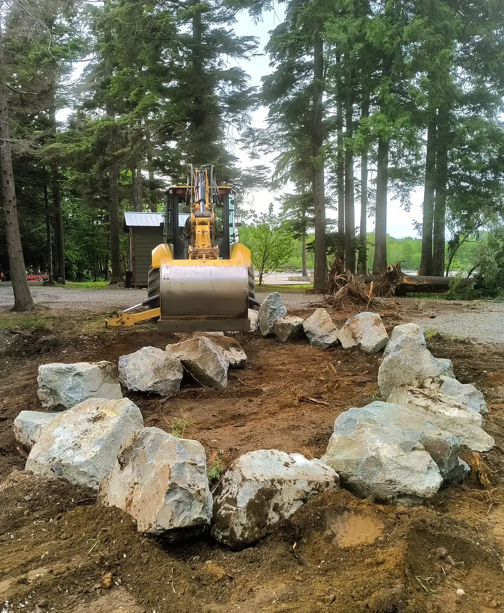 An excavator setting boulders into a ring on bare ground